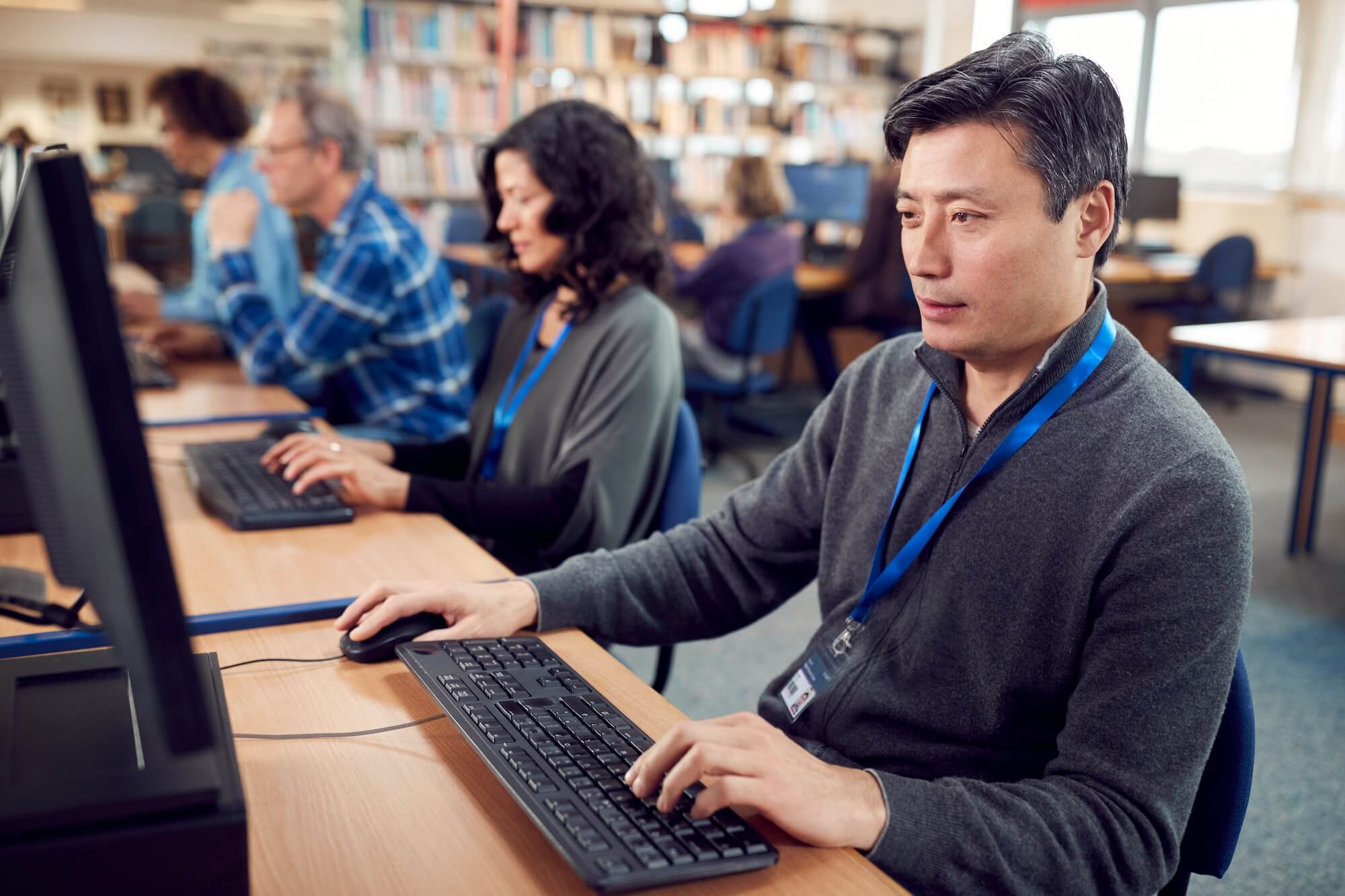 group of mature adult students in class working at computers in college library