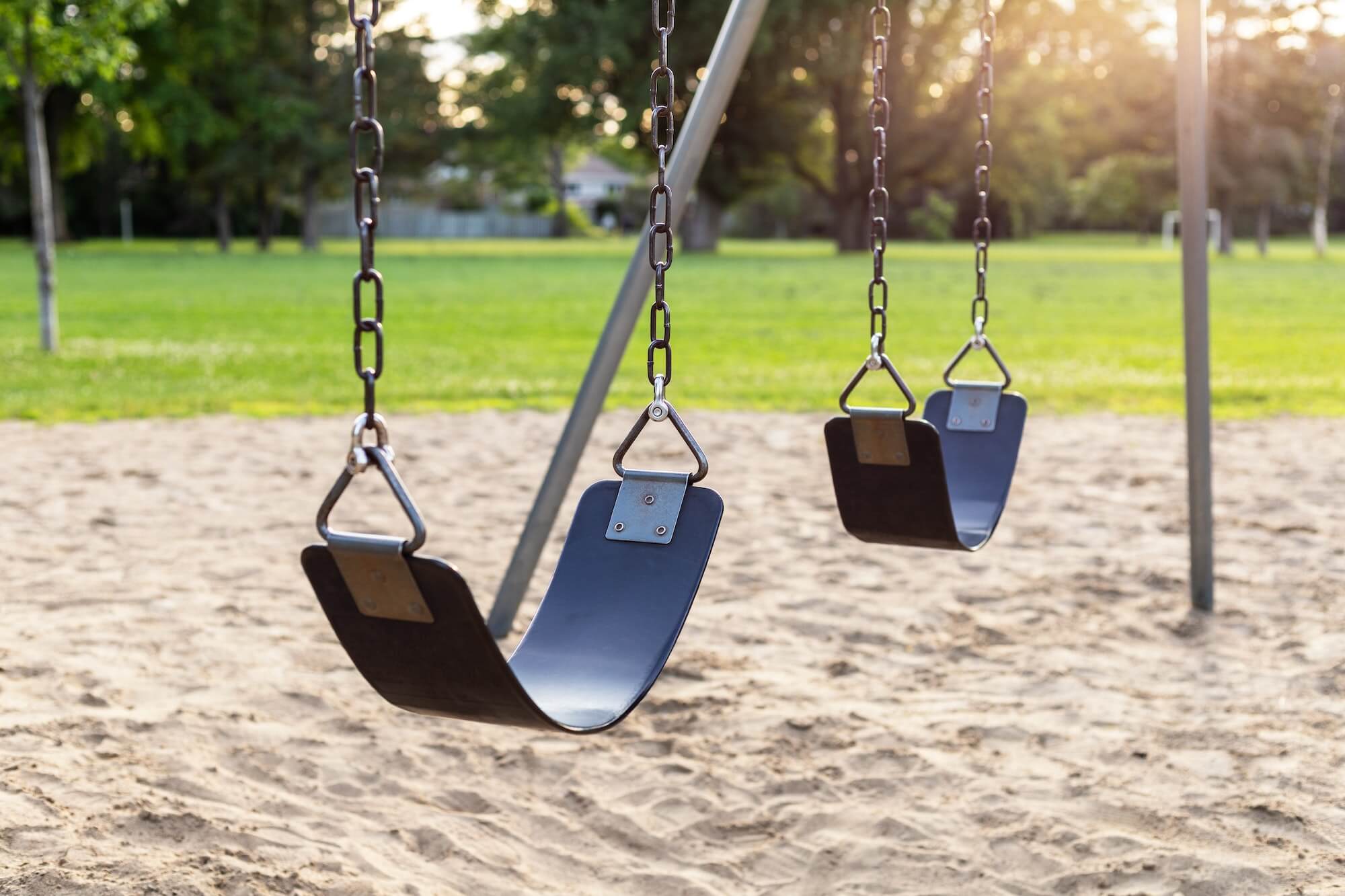 playground for children with swings in the public park near school yard during sunset